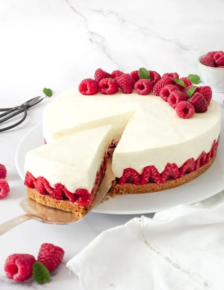 Cheesecake aux framboises sans cuisson sur une assiette garnie de framboises fraîches.