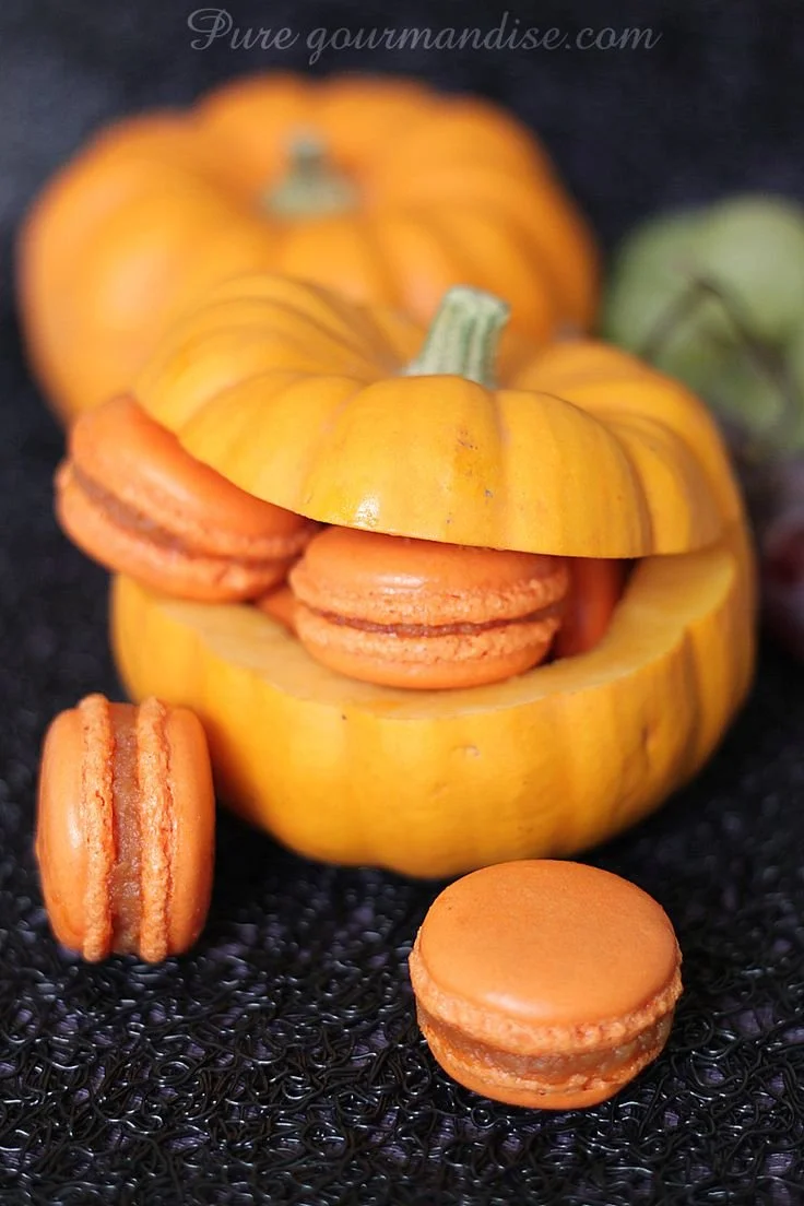 Macarons au potiron d'Halloween garnis de crème sucrée sur un plateau.